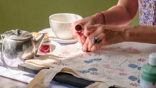 A close up of hands as they add the finishing touches to a colourfully printed tote bag.